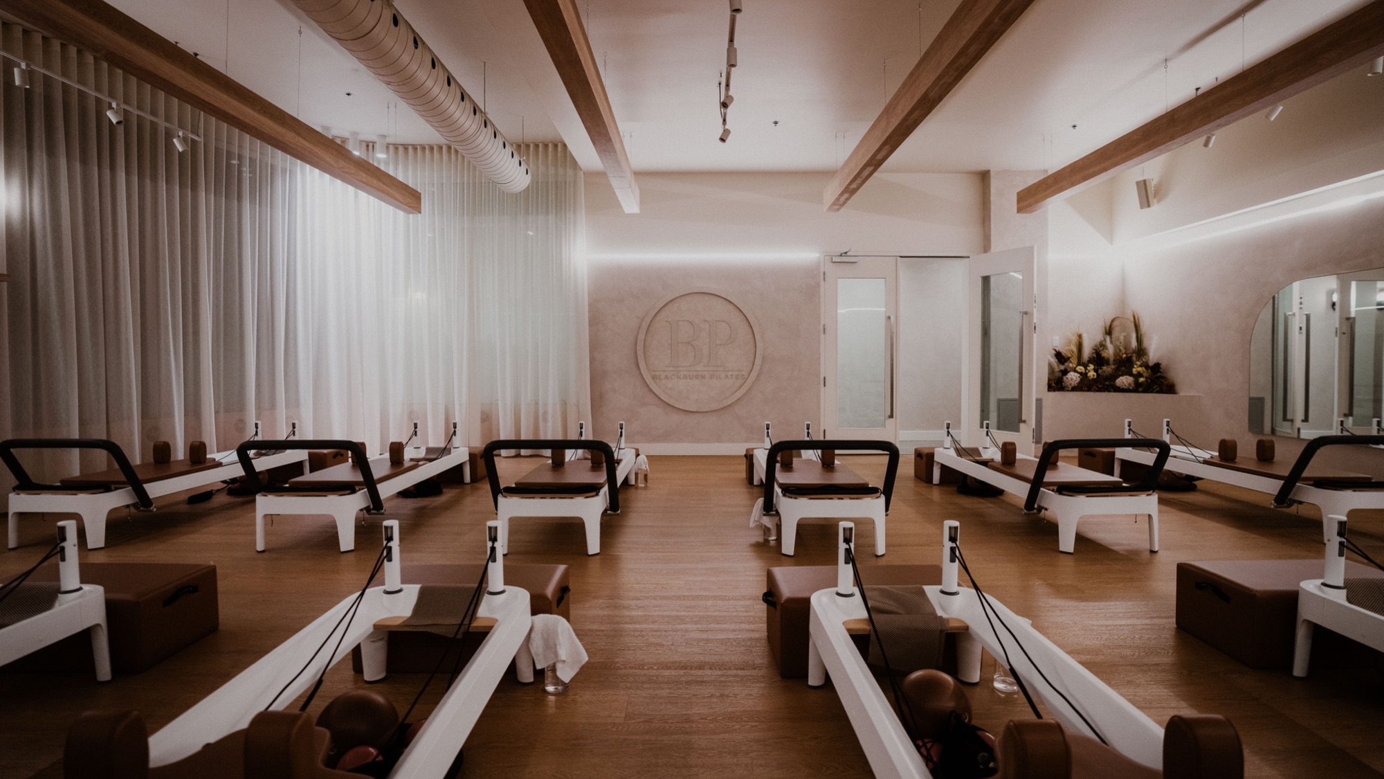 Plateau de reformers du studio Blackburn Pilates Sainte-Julie sous les poutres de bois, médaillon BP au mur